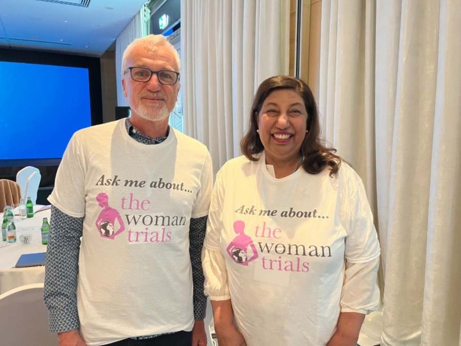 A man and woman smiling at the camera wearing t-shirts that say "Ask me about the WOMAN Trials"