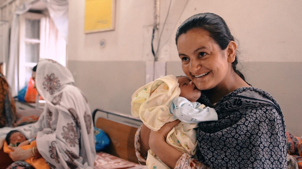 A smiling woman holds a newborn baby. 